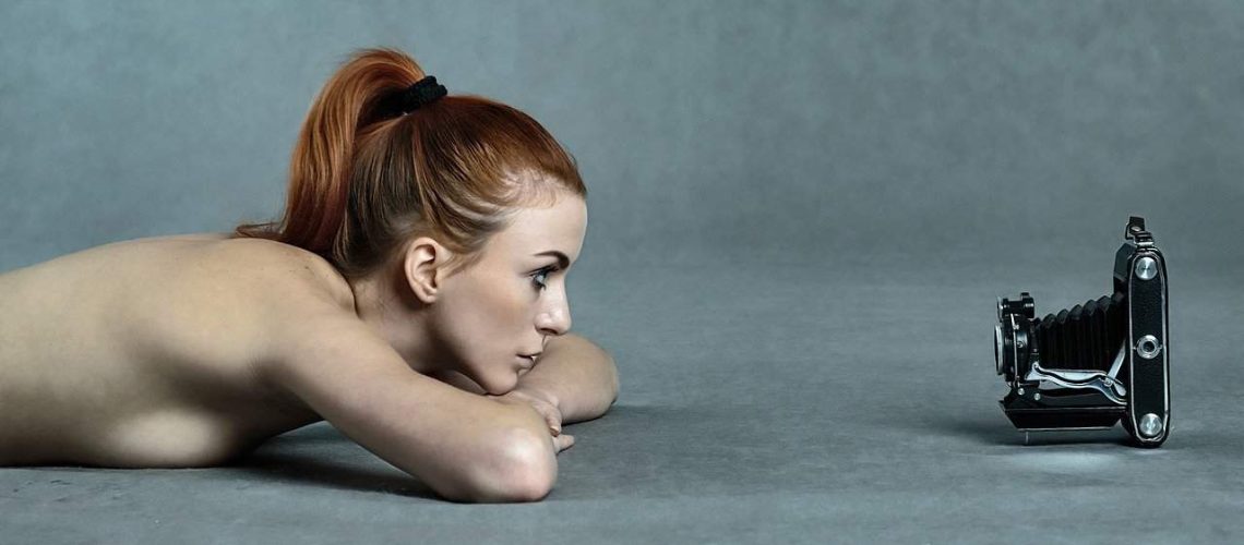 Naked woman lying on floor staring into a camera lens on the floor